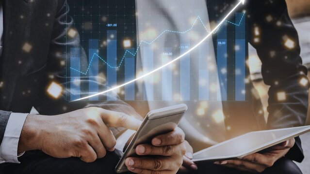 Two business professionals engage in financial analysis using a mobile device and tablet, with a dynamic growth chart and digital elements illuminating the workspace. Copula
