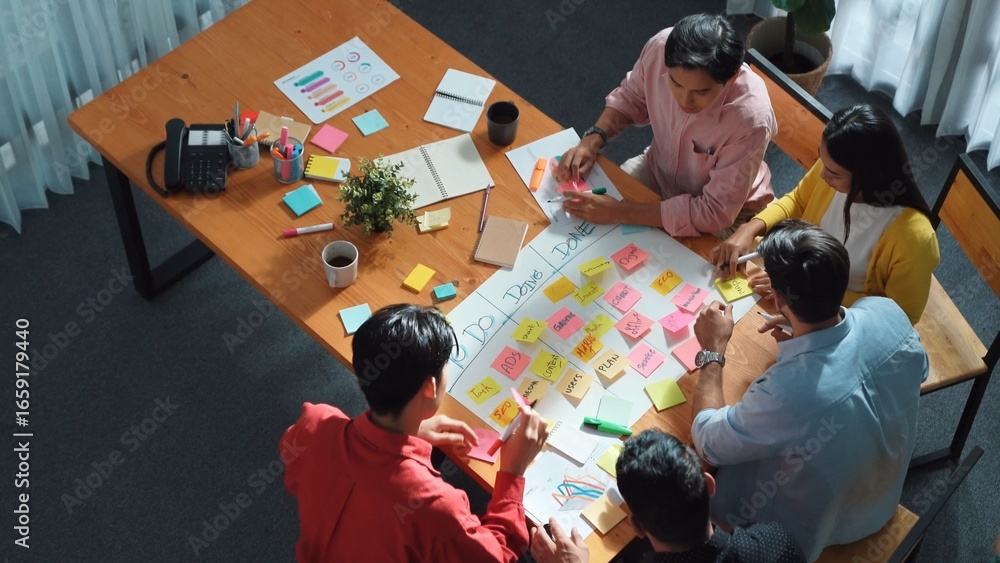 Poster close up of professional business team hands writing and putting sticky note on scrum task board. to