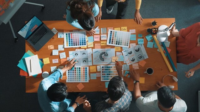 Top down view of designer compare color palettes with laptop and design product. Aerial view of marketing team working together to choose color while discussing about logo graphic design. Symposium.