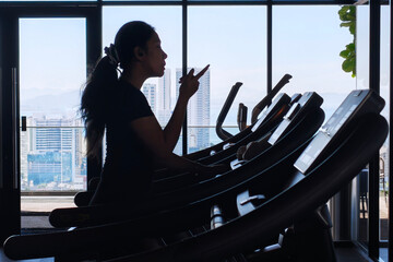 Silhouette of a woman exercising on a treadmill. A silhouette of a woman is exercising on a...