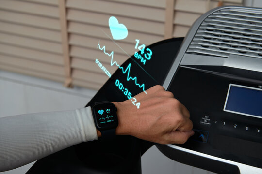 Person monitoring heart rate on a smartwatch with a futuristic hologram display while exercising on a treadmill at the gym.