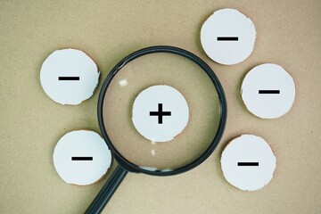 magnifying glass with minus and plus or positive and negative symbols. concept of comparing pros...