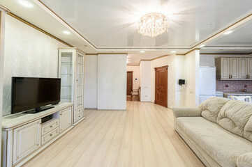 Elegant living room with light wood floors, a TV, cabinet, sofa, and a crystal chandelier. Warm, inviting space