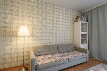 cozy room featuring a gray sofa with patterned blanket, a floor lamp, patterned wallpaper, and a...