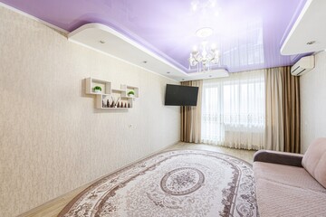 cozy living room with a lavender ceiling, a patterned oval rug, a TV, and neutral tones creates a...