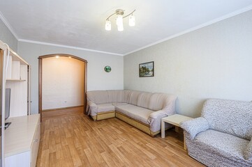 Cozy living room with a sectional sofa, armchair, wooden floor, and built-in shelving unit. Simple décor, warm lighting