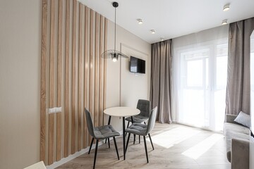 bright, modern apartment shows a round dining table surrounded by three grey chairs. A wooden slat...