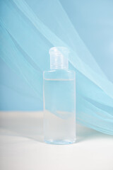 A transparent plastic bottle with a flip cap containing clear liquid, placed on a light surface with soft white fabric draped against a blue background.