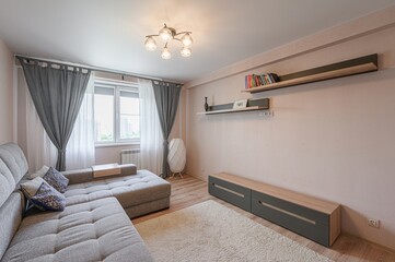 Cozy living room with a grey sectional sofa, soft rug, and floating shelves. The space is lit by a modern ceiling light and a unique floor lamp