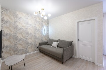 cozy room features a grey couch, textured walls, light wood floors, and a modern chandelier