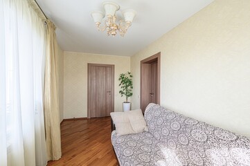 cozy room with a sofa, curtains, two doors, a plant, and a chandelier. The walls are light yellow,...