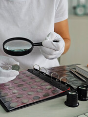 Coin collector examines valuable coins with magnifying glass