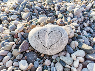 Heart-shaped design carved on a smooth stone surrounded by various pebbles on beach