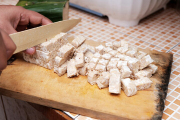 Close up of female hands cutting tempeh (made of soy beans) in small slices on wooden board. Tempeh is mainly used in Asian and vegetarian cooking.
