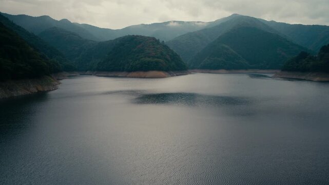 Serene Oku Tama Lake view with mountain ridges and cloudy atmosphere in Japan &ndash; Natural landscape scenery highlighting untouched greenery and water reflections.