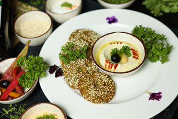 Home made hummus bowl, decorated with boiled chickpeas, herbs, pita and olive oil over a rustic metal background