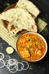 Paneer Butter Masala served with naan bread,onion rings and lemon, on a black background with space for text , Indian Curry