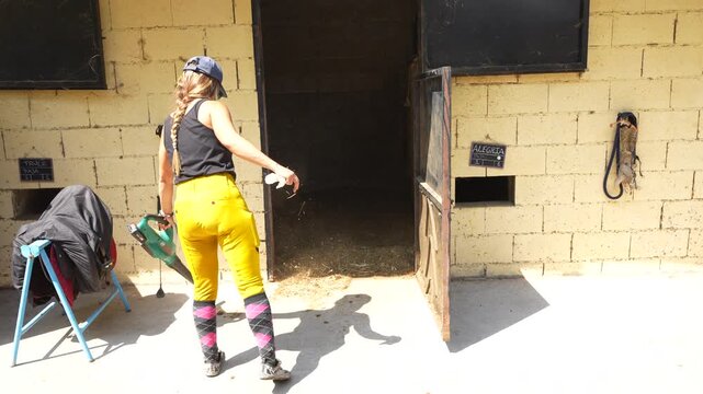 Female keeper uses a blower to push straw and dust into stalls while cleaning the stables exterior