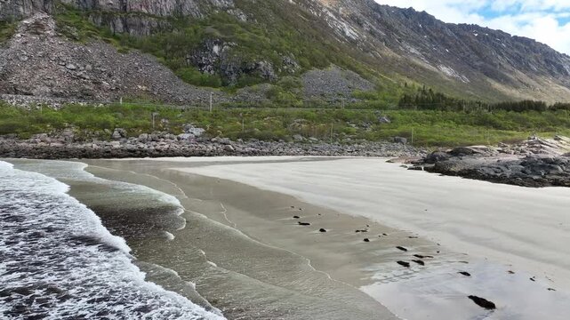 Aerial flying back over waves at Rorvik beach towards land with mountain and road in view