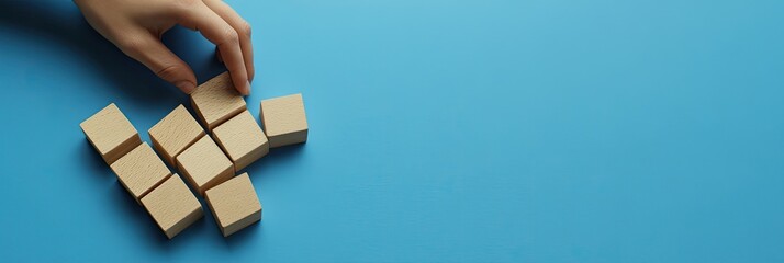 Photo of a hand holding wooden blocks to build steps on a blue background, representing a business growth and success concept.