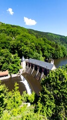 Panoramic view of a dam with lush surrounding forest and a clear sky