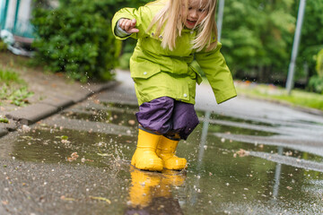 Little girl child in a raincoat and yellow rubber boots runs through puddles