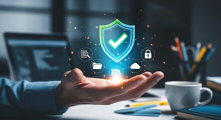 Hand holding a digital shield with checkmark surrounded by data protection icons on a desk background