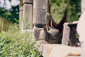 Rusty kettle resting on a wooden table surrounded by green plants in a peaceful outdoor setting