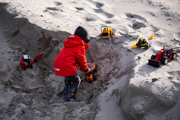 Child playing with toy trucks in the sand on a sunny day