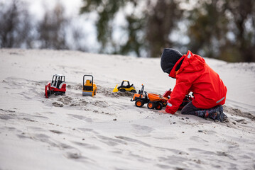 Child playing with toy trucks in the sand on a cold day