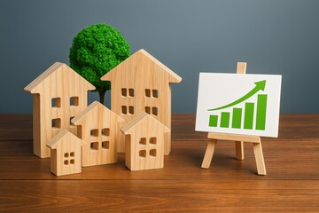 Wooden houses illustrate recovery, as a green graph on an easel signifies positive real estate market trends and optimistic future investment.