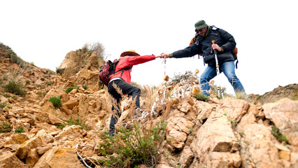 Help and mutual assistance in the mountains. A man pulls his friend to the top of a rocky hill....