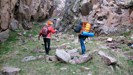 Two wanderers walk to the waterfall along a rocky gorge. Weekend camping trip. Tourists are hiking...