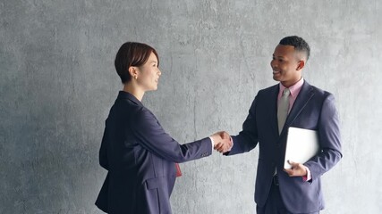 A black male businessman and a Japanese female staff member shaking hands in a stylish room