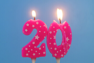 Pink birthday candles with stars burning on blue background, number 20.	
