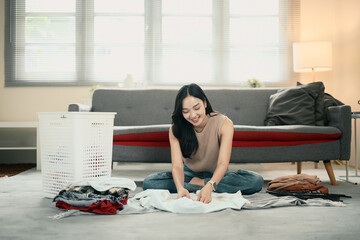 Female doing household chores, sorting and folding fresh laundry on the floor at home