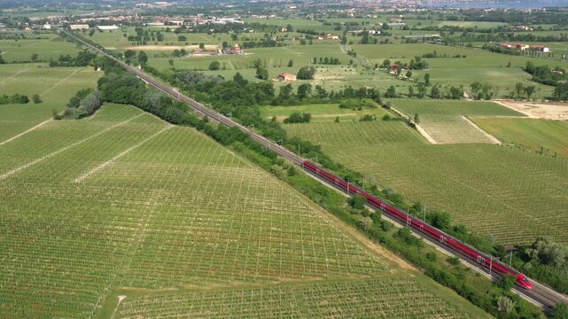 A high-speed train glides through Italian vineyards, its motion frozen in a stunning aerial perspective. A perfect travel moment.