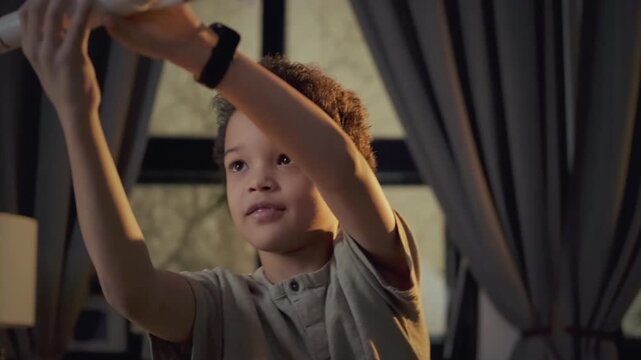 Medium close-up portrait of joyful Black boy having fun playing with toy space rocket in evening