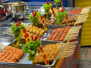 Bangkok, Thailand - June 26, 2025: Rows of skewered meat and sausages decorated with lettuce at a...