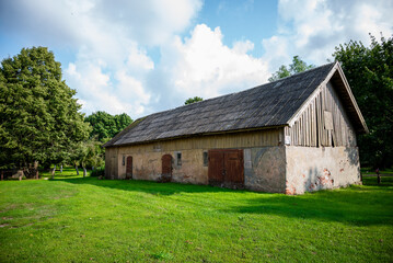 Obraz premium Rural farm building with a wooden gabled roof and plastered stone foundation shows signs of weathering and age. 