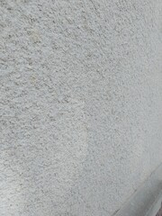 A close-up of a rough, light gray stucco wall surface with a grainy and uneven texture.