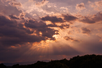 夕暮れ時の雲の間から漏れる夕日の光芒