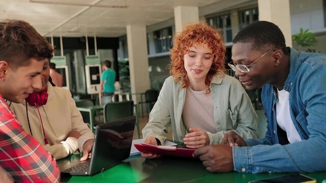Happy diverse young university students studying together for exams with notes, cell phone and laptop at college library