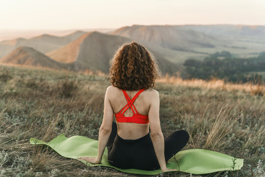 Woman sitting in a yoga pose, a hilly landscape at sunset