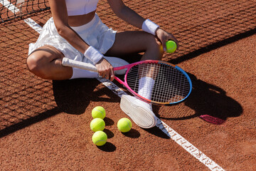 Female tennis player seated on clay court with racket and balls during practice