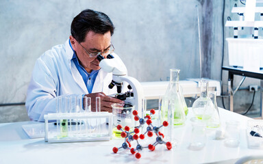Scientist using a microscope at a lab bench with test tubes, flasks, and a molecular model, representing laboratory research, analysis, and innovation in modern science.