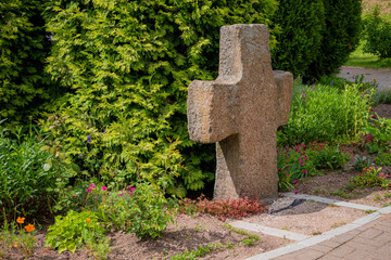 A weathered granite cross is enveloped in lush greenery and blooming flowers, exuding calm