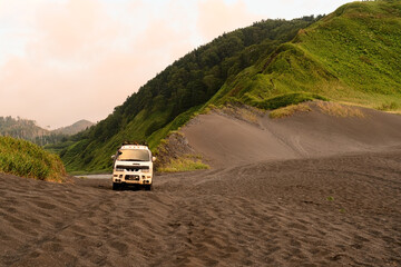 Durable expedition vehicle standing alone at untouched beach with dramatic mountain ridges meeting...