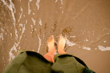 Close overhead shot of woman's feet being washed by gentle ocean waves on sandy beach. Perfect...