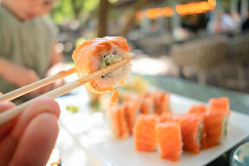 Mouthwatering close-up of fresh salmon and cucumber sushi roll held with chopsticks, showcasing...
